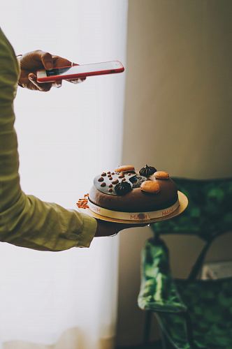 person holding iPhone taking photo of cake near curtains